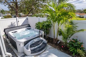 Ein Whirlpool mit einer Leiter, umgeben von einem weißen Zaun, Palmen und verschiedenen Pflanzen.