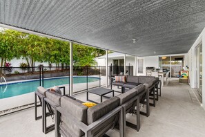 Ein überdachter Außenbereich mit Pool, Sitzgelegenheiten und Blick auf ein Haus.