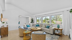 A spacious living room with a large sofa, a coffee table, and a wicker chair. There is a view of the outside through large windows. - Breezy Blue-pool Hot Tub Minutes to Beach Games (Largo)