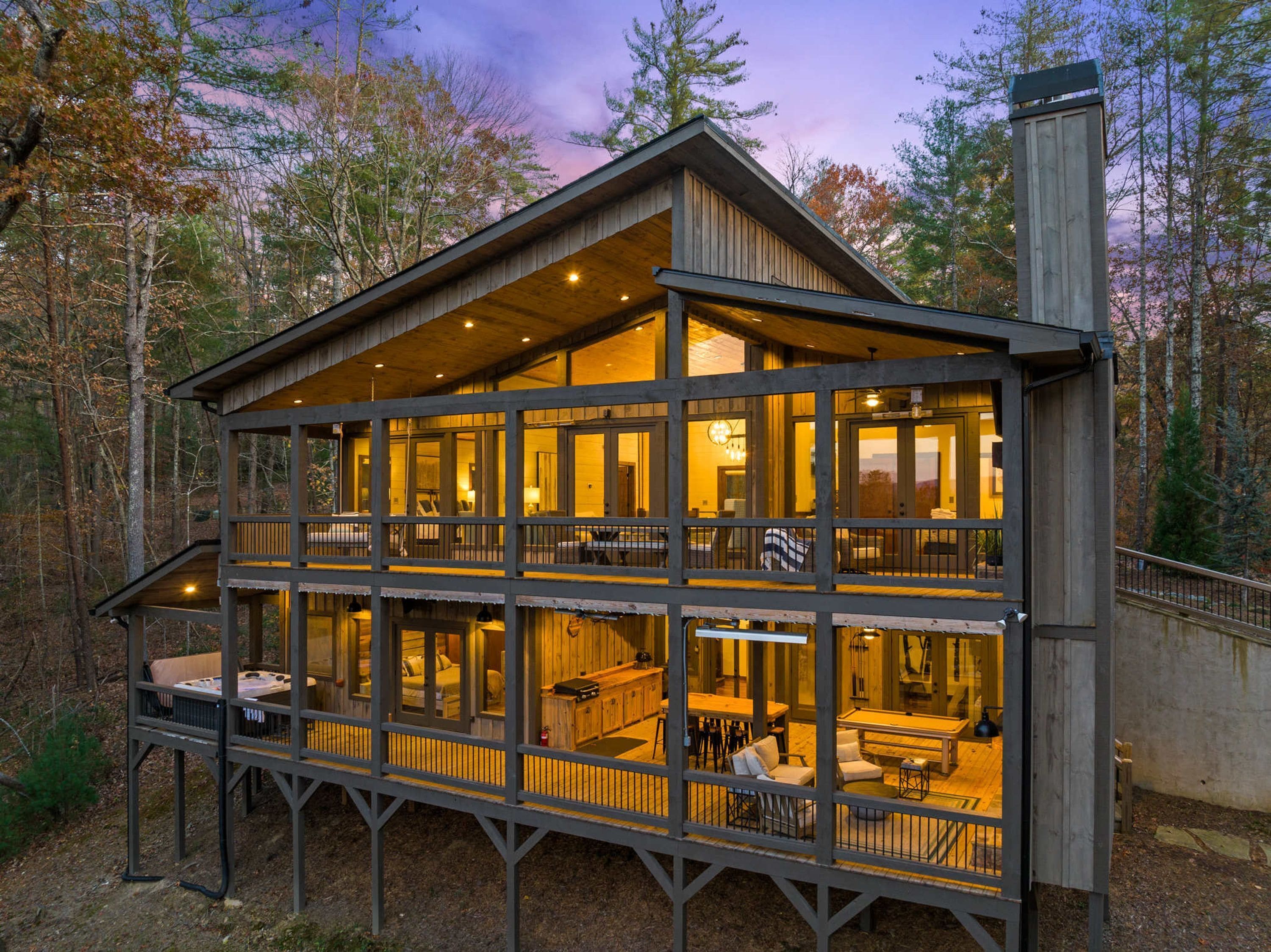 Een chalet met twee verdiepingen, een balkon, grote ramen en een open haard.
