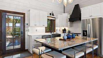A modern kitchen with white cabinetry, a large island with seating, a stainless steel refrigerator, and a black range hood.