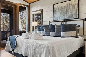 A neatly made bed with a quilted white cover, a stack of white towels, and a view of a forest through a glass door. - 2-level Deck - Stunning Views - Hot Tub - Fire Pit (Ellijay)
