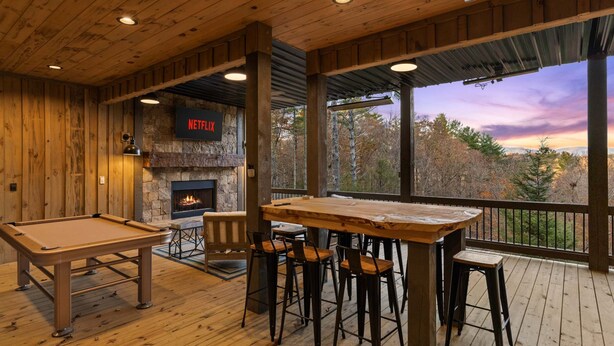 A wooden interior with a pool table, bar stools, a fireplace, and a large window overlooking a forest. - 2-level Deck - Stunning Views - Hot Tub - Fire Pit (Ellijay)