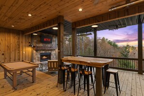 A wooden interior with a pool table, bar stools, a fireplace, and a large window overlooking a forest. - 2-level Deck - Stunning Views - Hot Tub - Fire Pit (Ellijay)