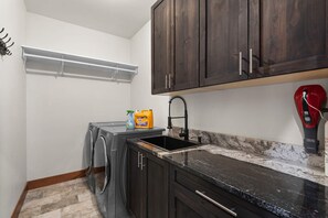 A compact kitchen with a built-in washer and dryer, a sink with a modern faucet, and dark wooden cabinets. - 34 Acre Escape Games Hiking Pool Table Bicycles (Black Hawk)