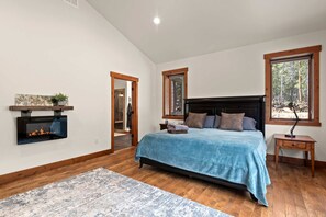Ein Schlafzimmer mit einem Bett, einem Nachttisch, einem Kamin und einem Fenster mit Blick auf Bäume.