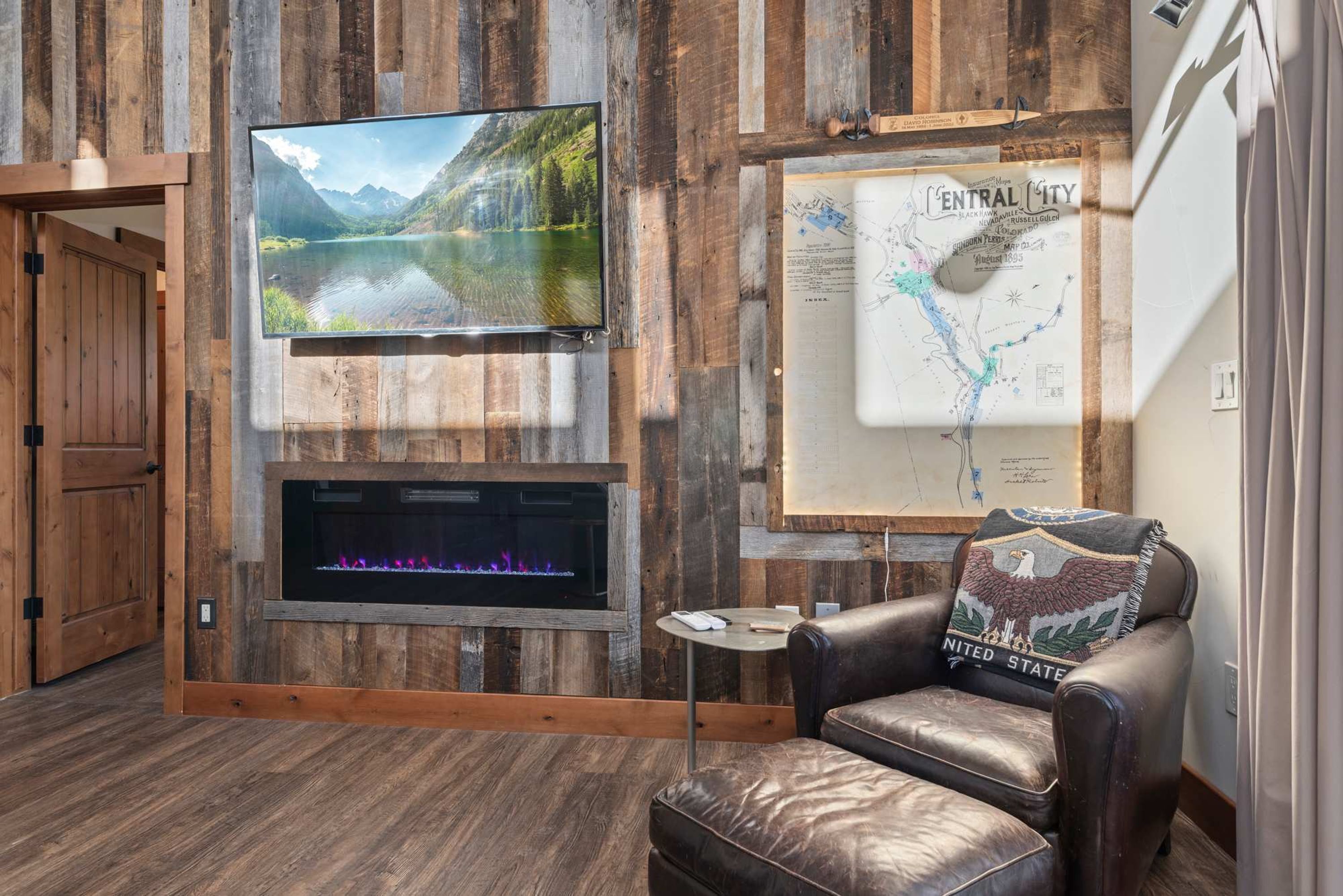 Habitación con pared de madera, televisor montado, chimenea, mapa y sillón de cuero.