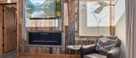 A room with a wooden wall, a mounted television, a fireplace, a map, and a leather chair.