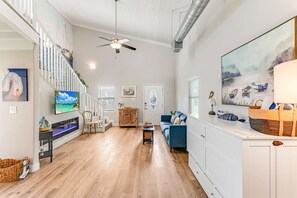 Ein geräumiger Wohnbereich mit Holzboden, einem blauen Sofa, einem Fernseher und Kunstwerken an den Wänden.