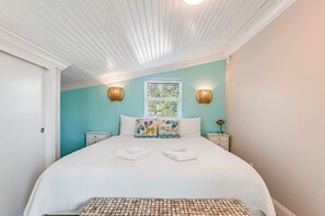 Ein Schlafzimmer mit einem Bett, zwei Nachttischen, einem Fenster mit Jalousien und einer Decke mit Holzbalken.