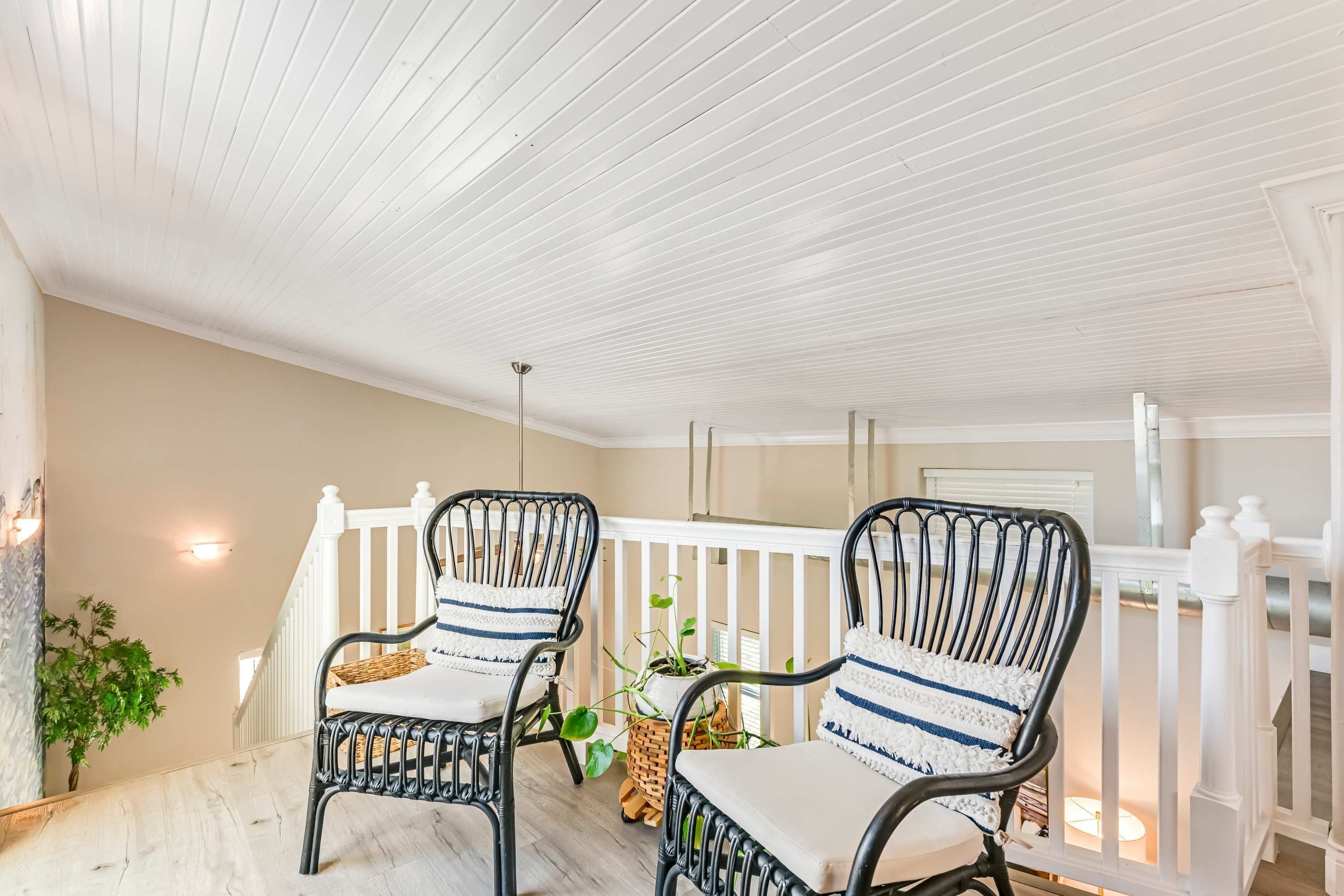 A covered porch with two wicker chairs, a white railing, and a ceiling with horizontal beams.