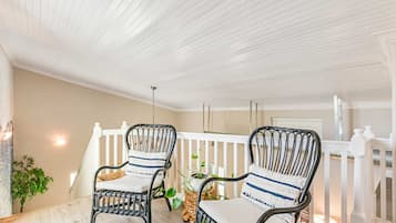 A covered porch with two wicker chairs, a white railing, and a ceiling with horizontal beams.
