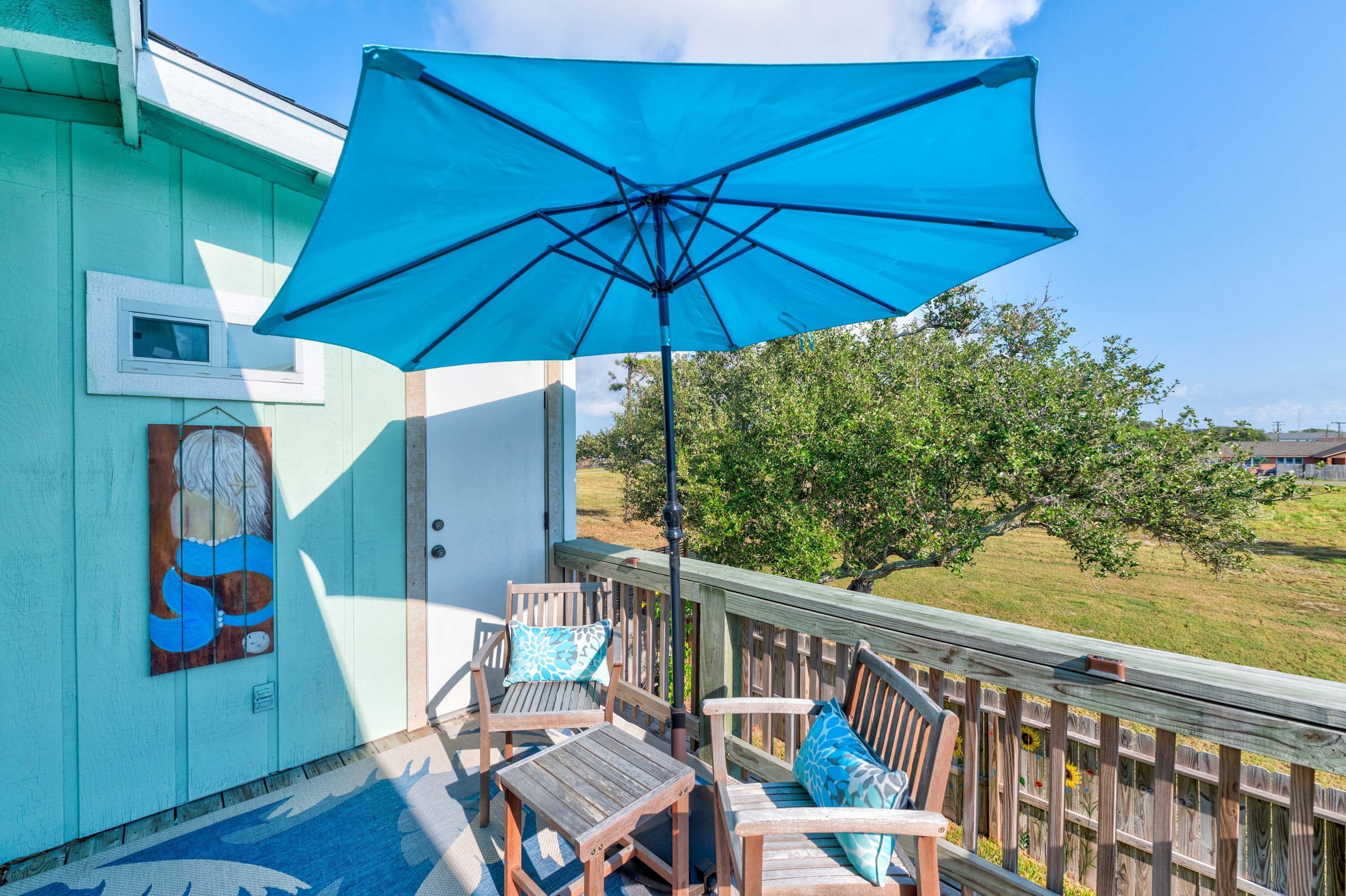 Une terrasse en bois avec un parasol bleu, deux chaises en bois et une petite table.