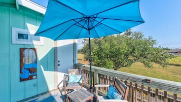 Une terrasse en bois avec un parasol bleu, deux chaises en bois et une petite table.