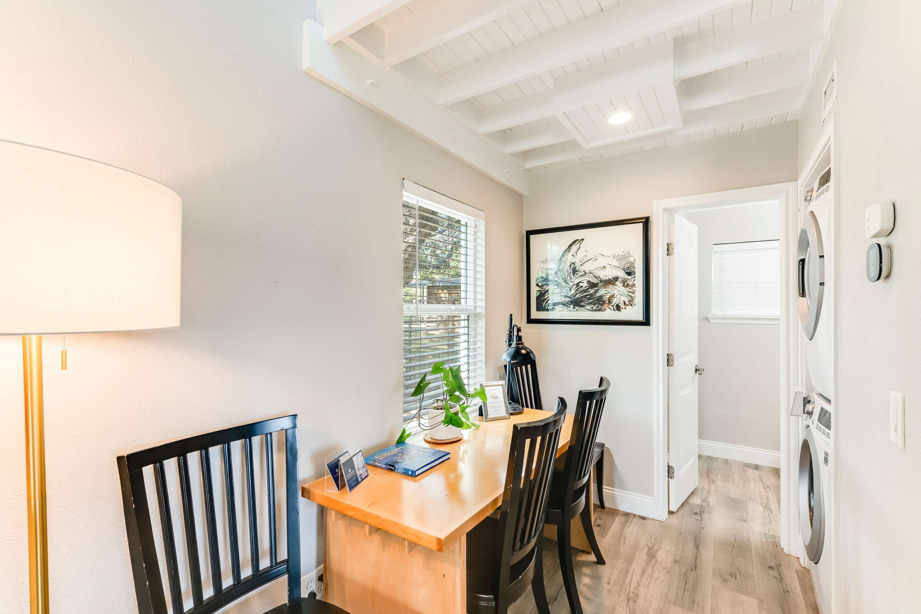 Un coin repas avec une table en bois, des chaises noires, une lampe et un tableau encadré au mur.