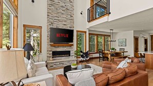 A spacious living room with a stone fireplace, a large flat-screen TV mounted above it, and a cozy seating area with leather sofas. - 2 Homes Sleeps 22 Sauna Hot Tub Fire Pit (Government Camp)