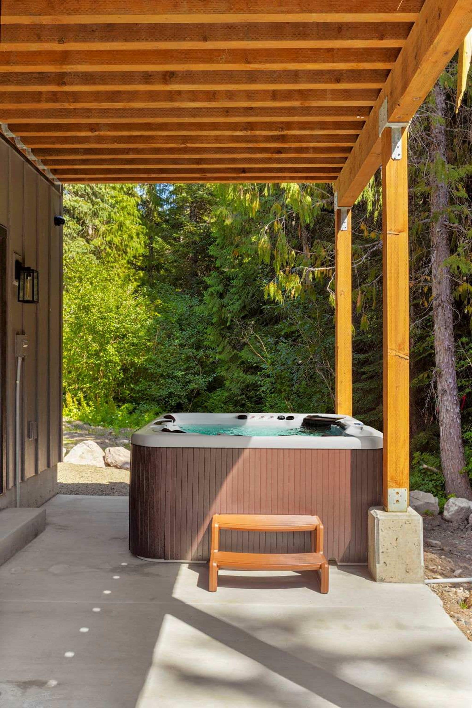 Un jacuzzi bajo una pérgola de madera con un banco, rodeado de vegetación.