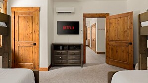 A hotel room with a bed, a TV mounted on the wall, a wooden wardrobe, and a hallway with wooden doors.