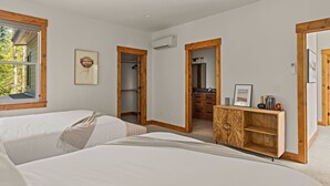 A bedroom with two beds, a wooden wardrobe, a framed picture on the wall, and a window with a view of trees. - 2 Homes Sleeps 22 Sauna Hot Tub Fire Pit (Government Camp)