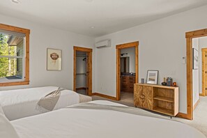 Un dormitorio con dos camas, un armario de madera, un baño con espejo y una ventana con vistas a árboles.