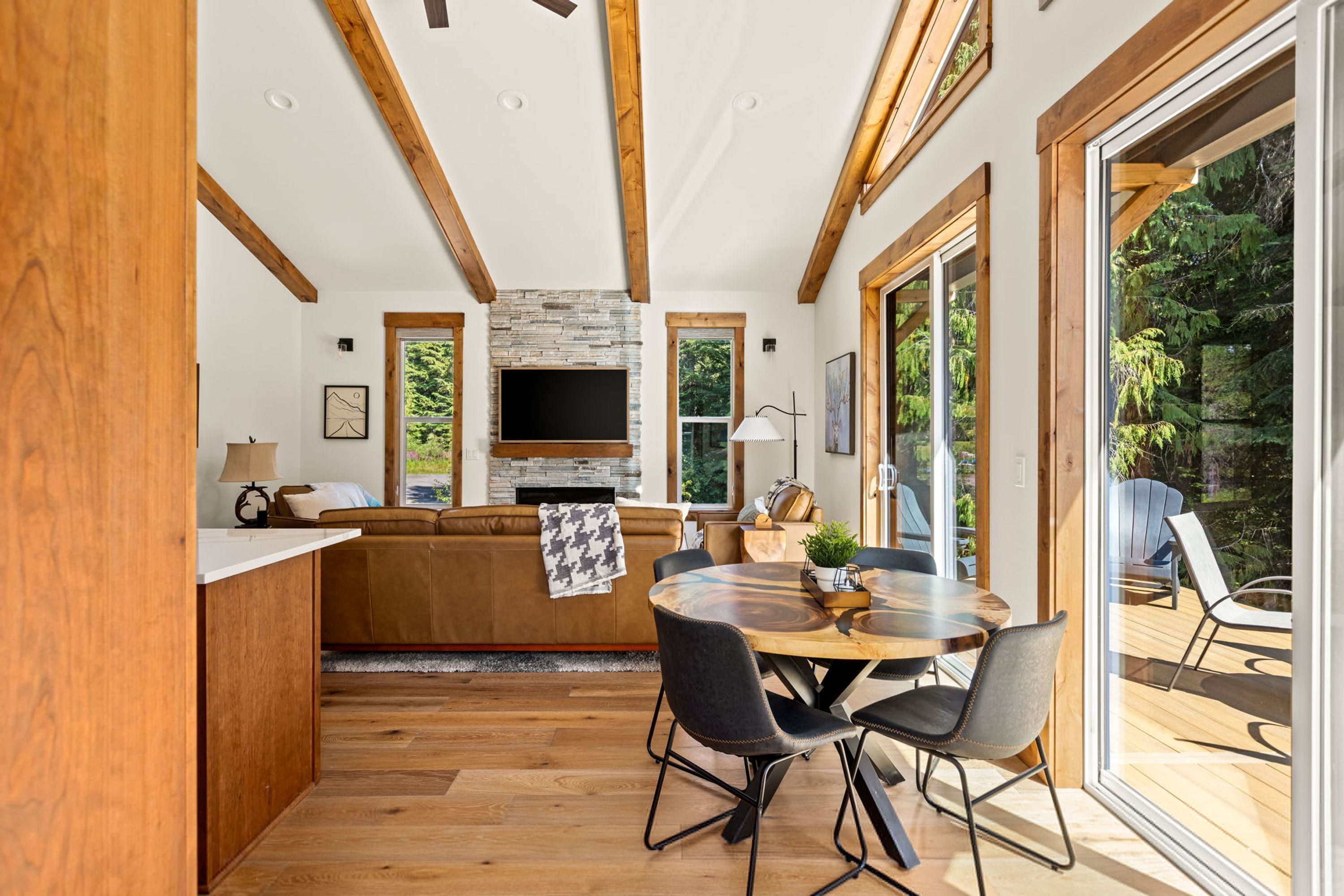 Un interior moderno con techo de madera, chimenea de piedra, una mesa de comedor redonda y vistas al exterior.