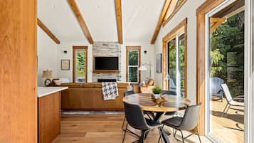Un interior moderno con techo de madera, chimenea de piedra, una mesa de comedor redonda y vistas al exterior.