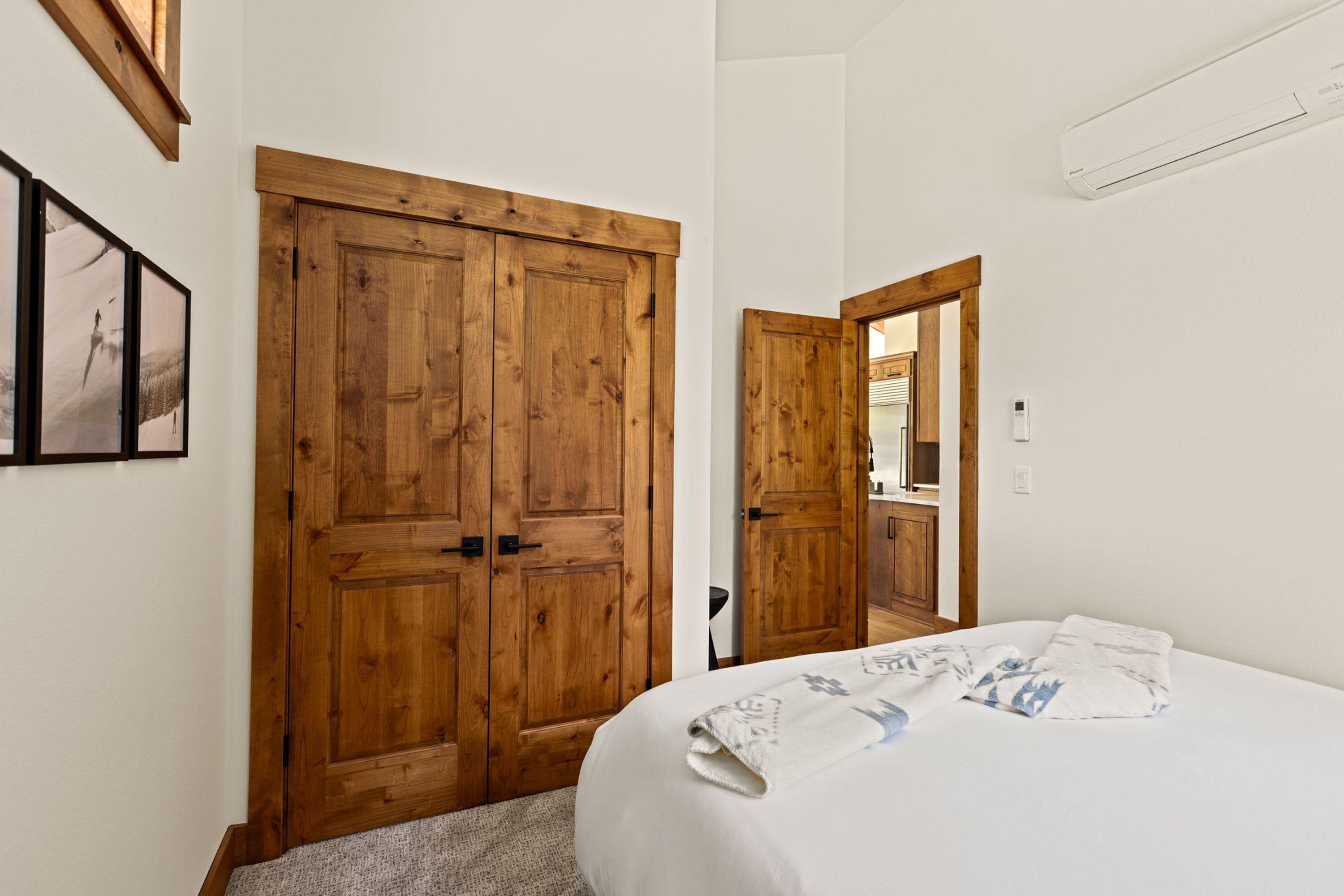 A bedroom with a large wooden wardrobe, a bed with a white duvet, and a wall-mounted air conditioner.