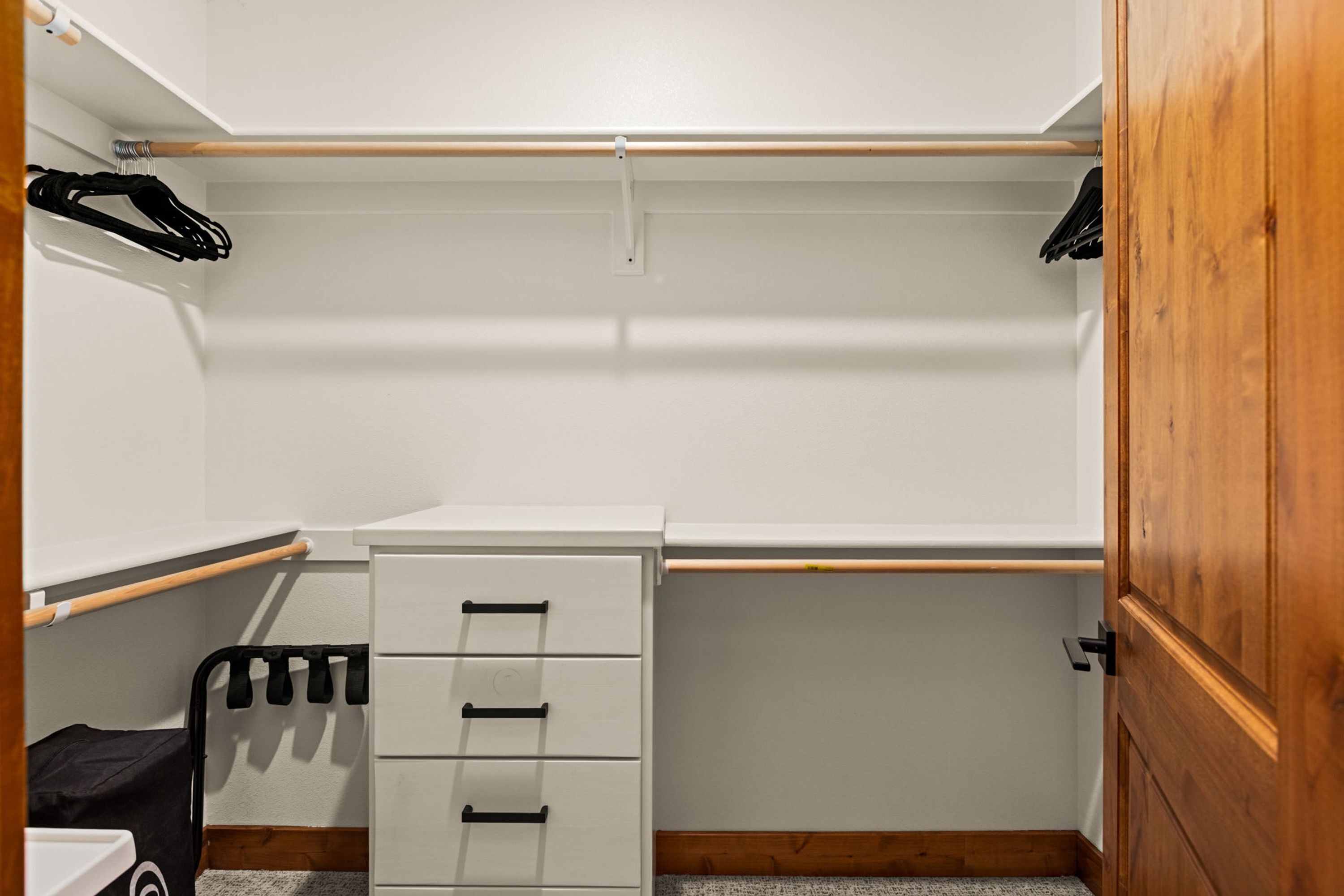 A walk-in closet with a wooden door, a white storage unit with drawers, and a shoe rack.