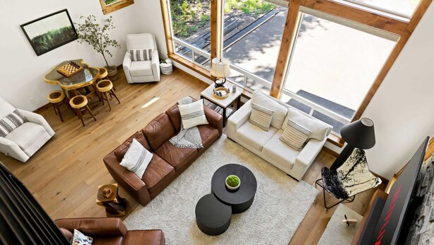 A spacious living area with a large window, a brown leather sofa, a white sofa, a round coffee table, and a chess table. - 2 Homes Sleeps 22 Sauna Hot Tub Fire Pit (Government Camp)