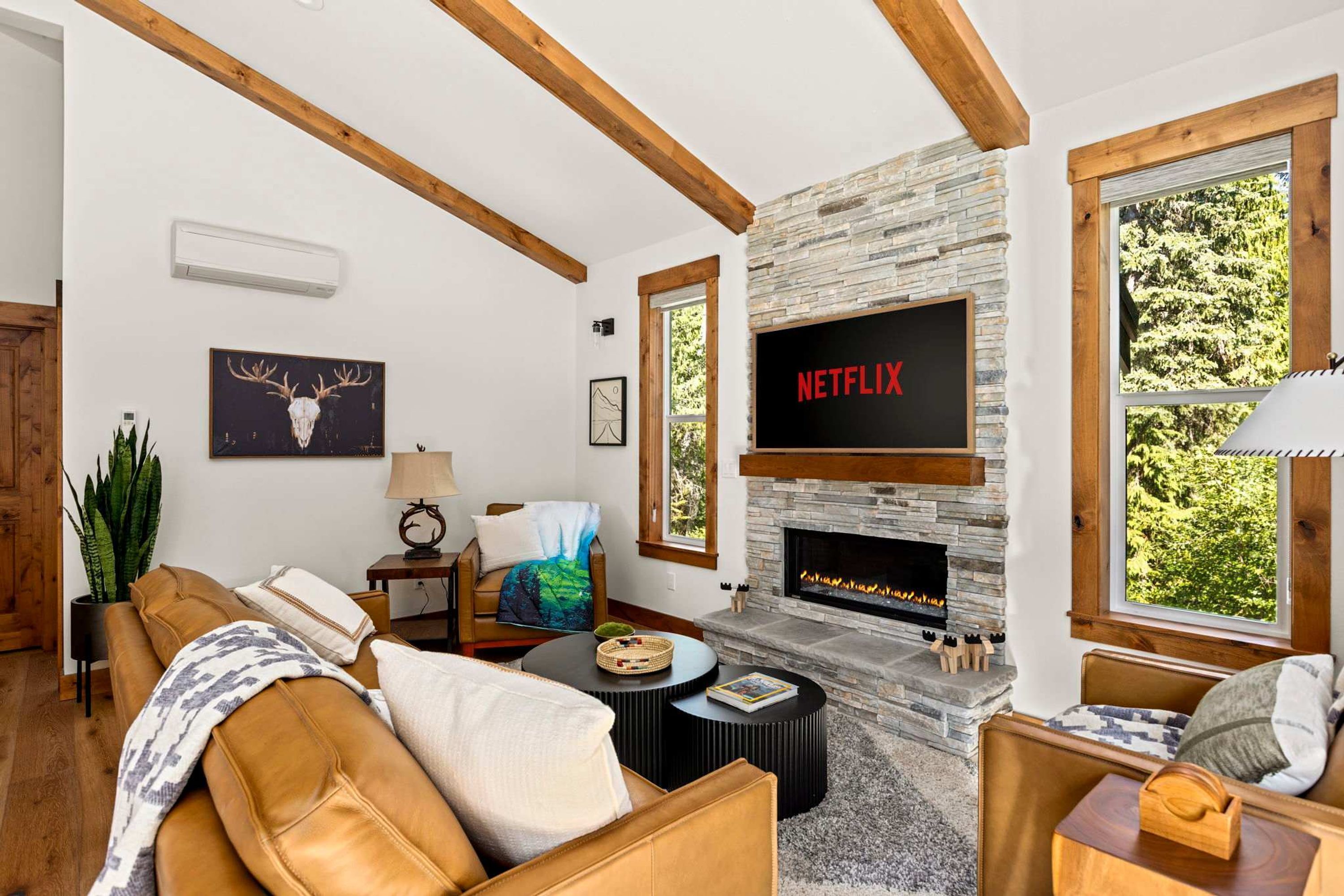 Una sala de estar acogedora con chimenea de piedra, un televisor montado sobre ella y un amplio ventanal con vistas al follaje.