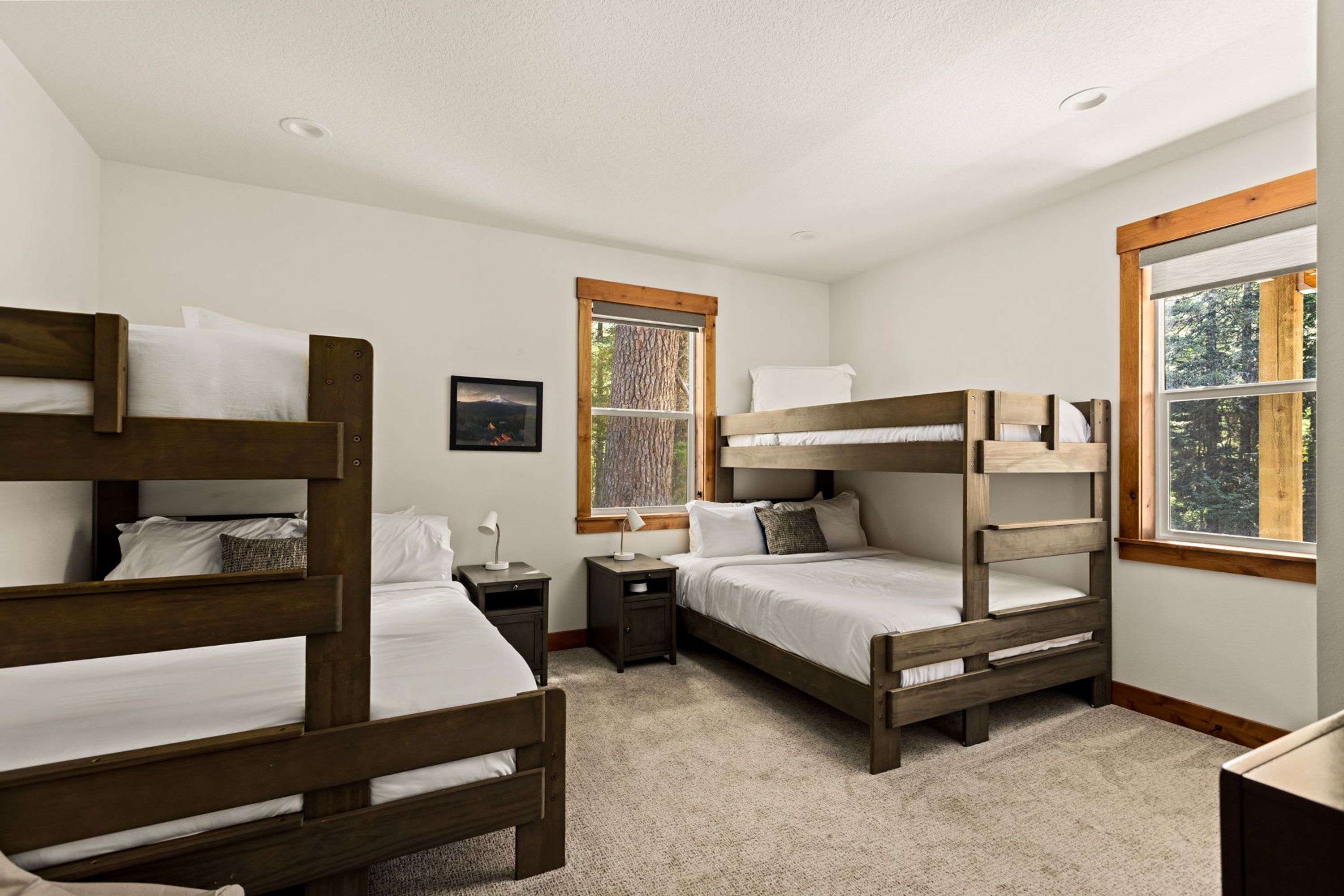 A bedroom with bunk beds, a window with a view, a nightstand, and a framed picture on the wall.