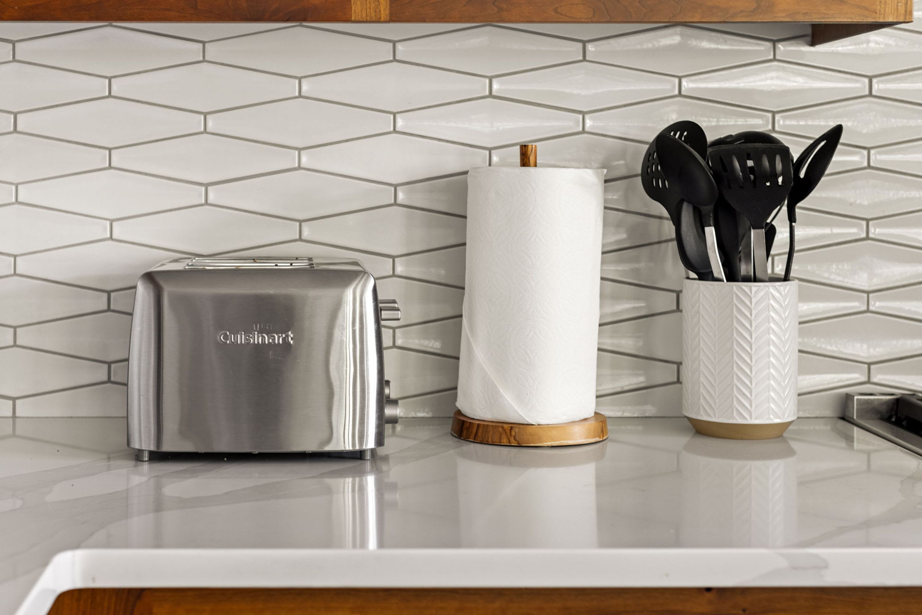 Una encimera de cocina con un tostador Cuisinart, un rollo de toallas de papel y un portalapices con utensilios negros.