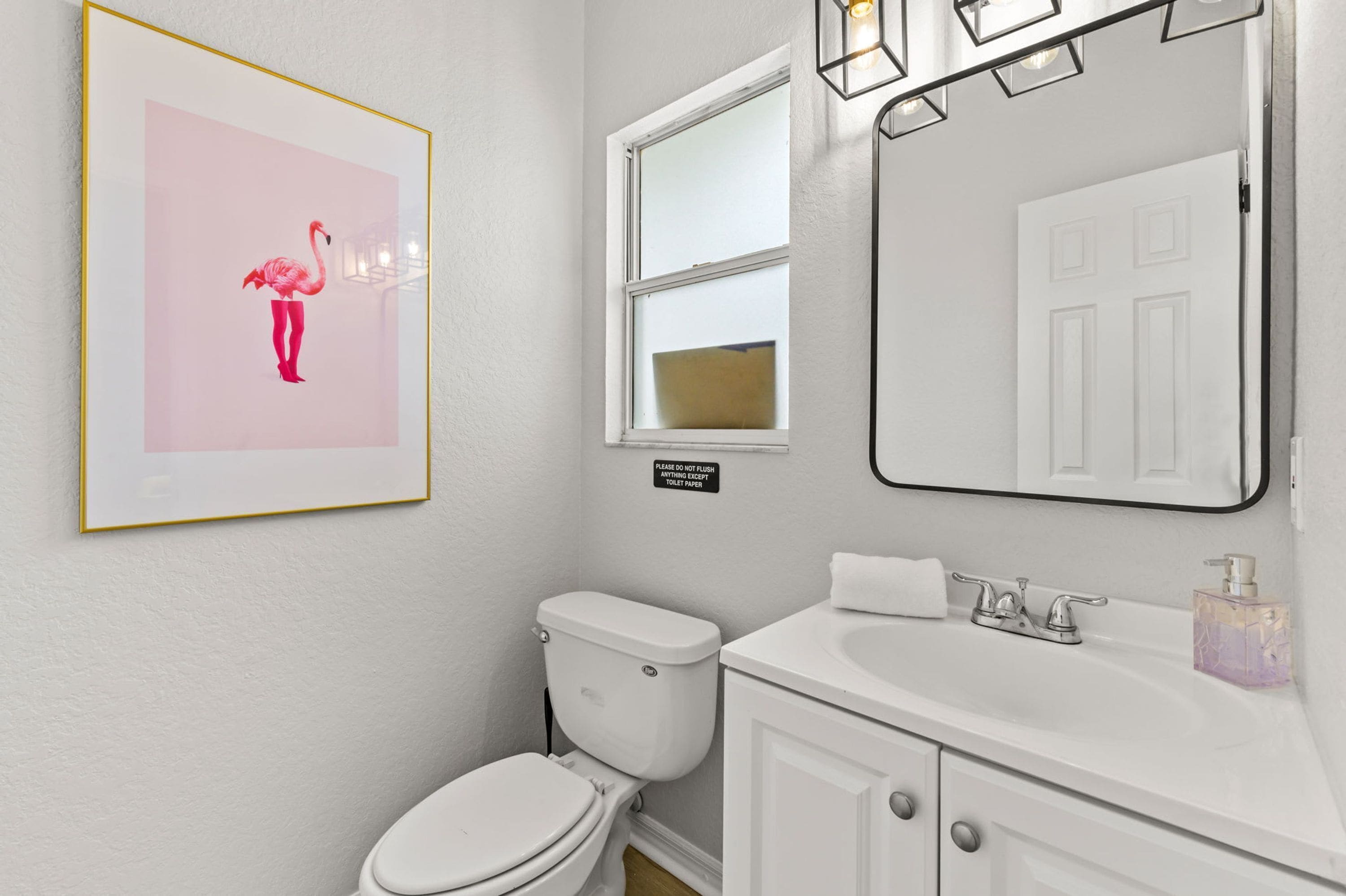 A bathroom with a toilet, sink, and a framed picture on the wall.