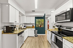 Una cocina moderna con armarios blancos, un microondas, una cafetera y un lavamanos.