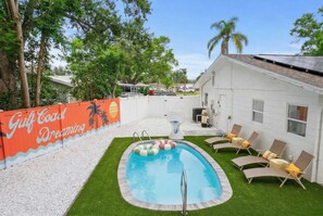 Um quintal com piscina, um edifício branco e uma cerca com pintura de palmeiras.