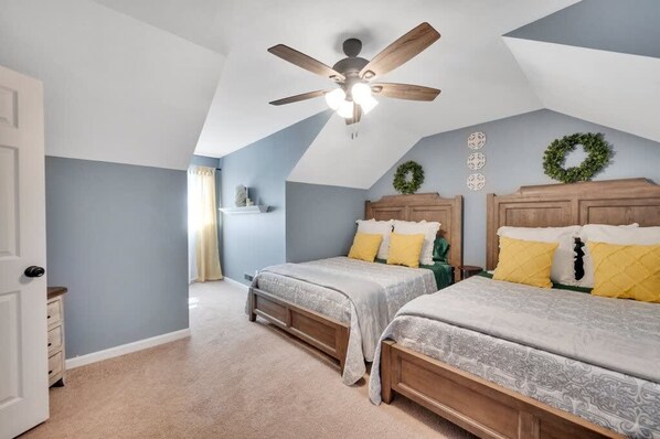 Quarto com duas camas, ventilador de teto e teto inclinado.
