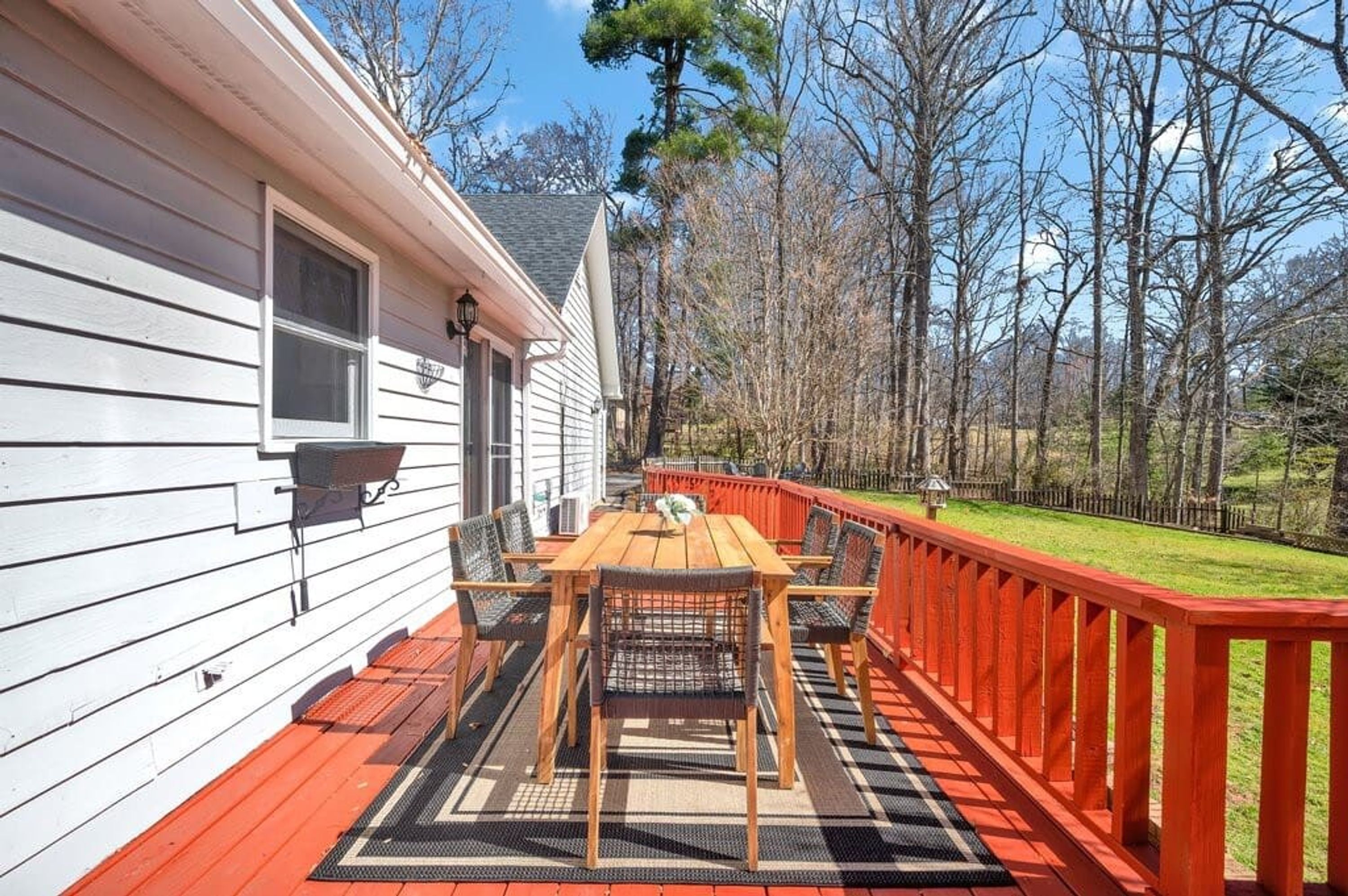 A wooden deck with a table and chairs, a red railing, and a house with white siding.