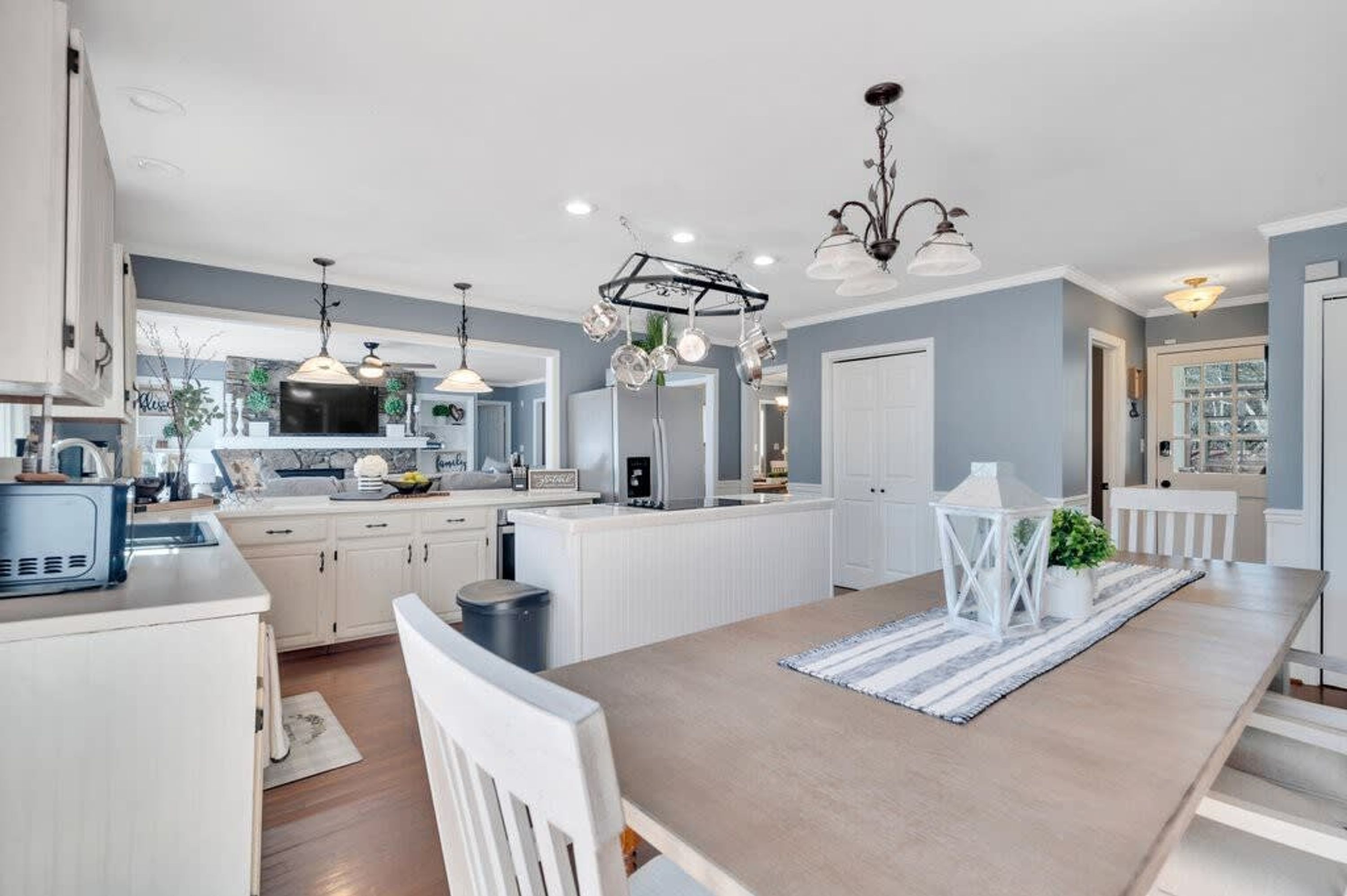 A modern kitchen with white cabinetry, a central island, pendant lighting, and a view to the outside.