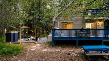 A house with a deck, a swing set, and a small outdoor seating area.
