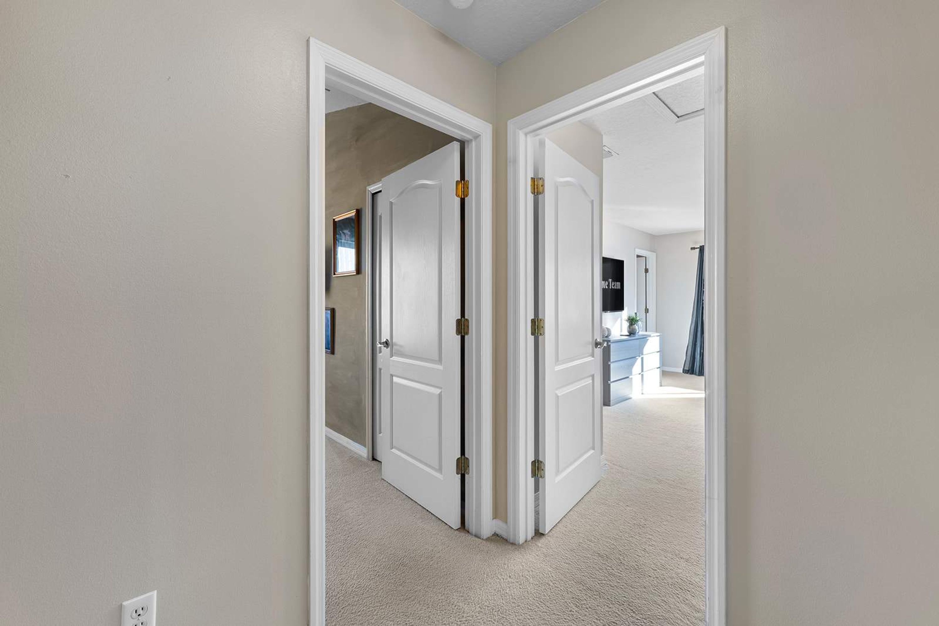 A hallway with white doors leading to a room with a blue accent wall and a visible bathroom.