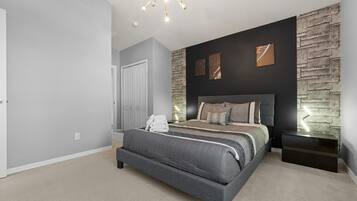 Un dormitorio con cama, mesita de noche, lámpara de pared y una puerta.