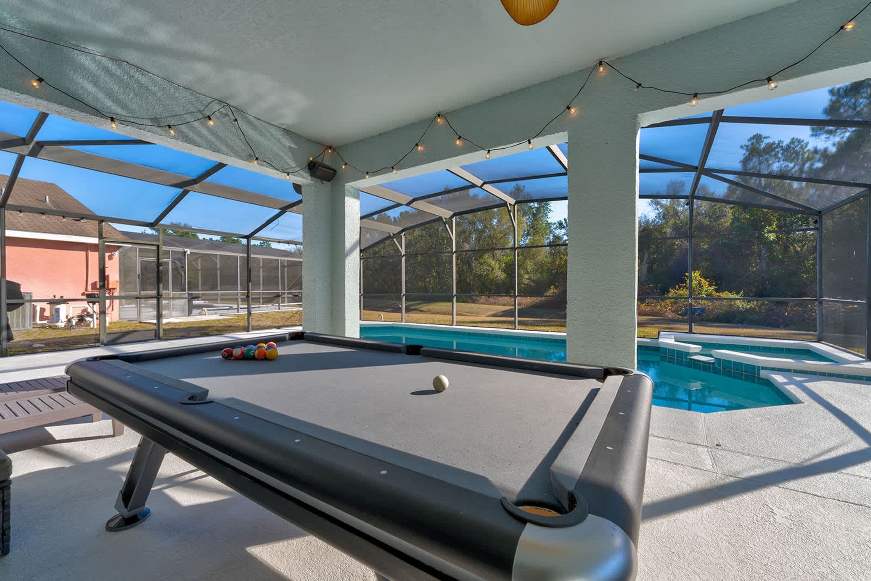 A pool table with a netted enclosure, a pool, and a clear view of the outdoors.