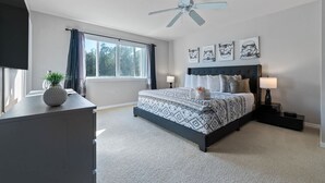 Um quarto com uma cama grande, um ventilador de teto, uma janela com cortinas e obras de arte na parede.