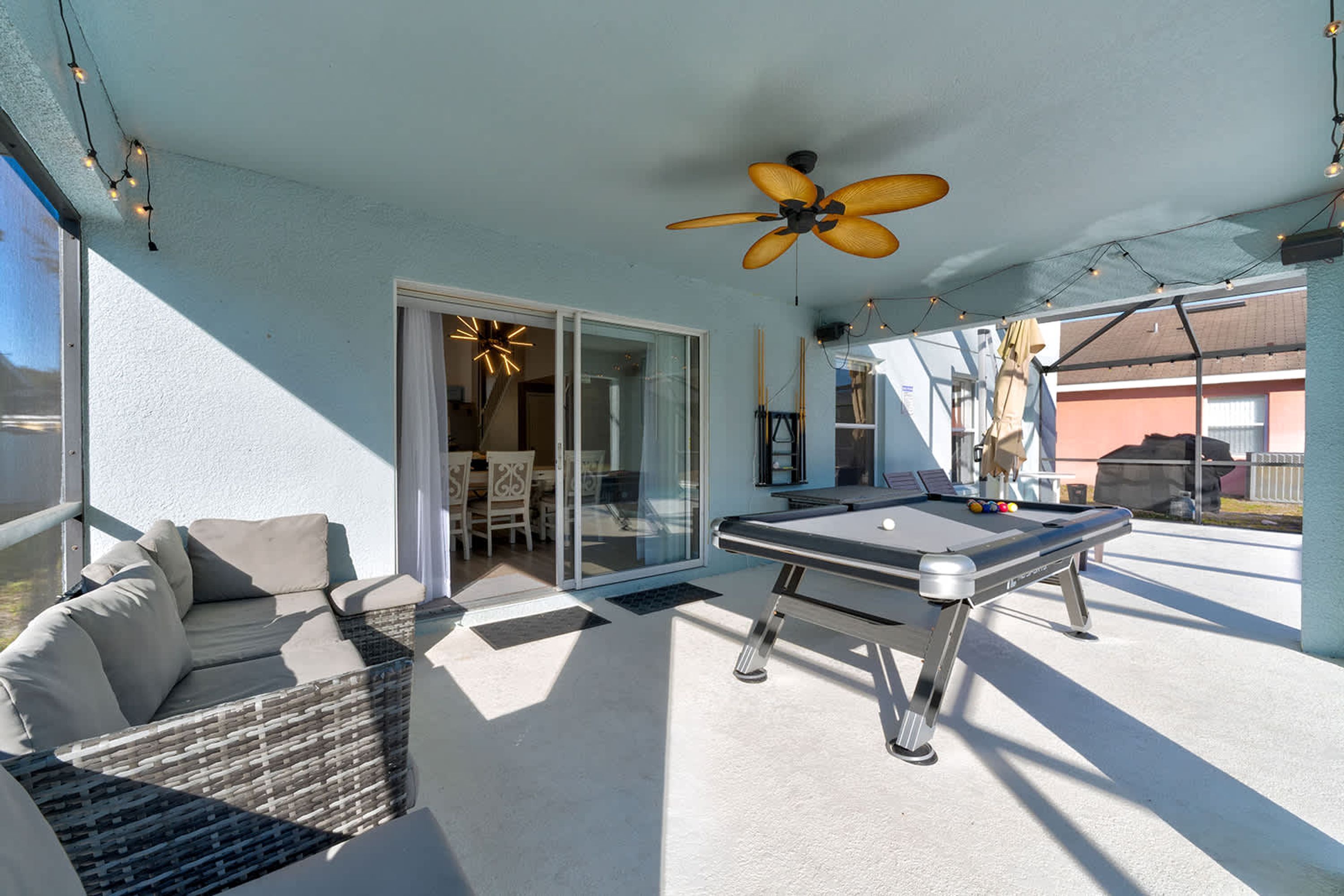 An outdoor patio with a pool table, a ceiling fan, and a seating area with cushions.