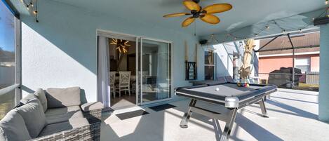 An outdoor patio with a pool table, a ceiling fan, and a seating area with cushions.