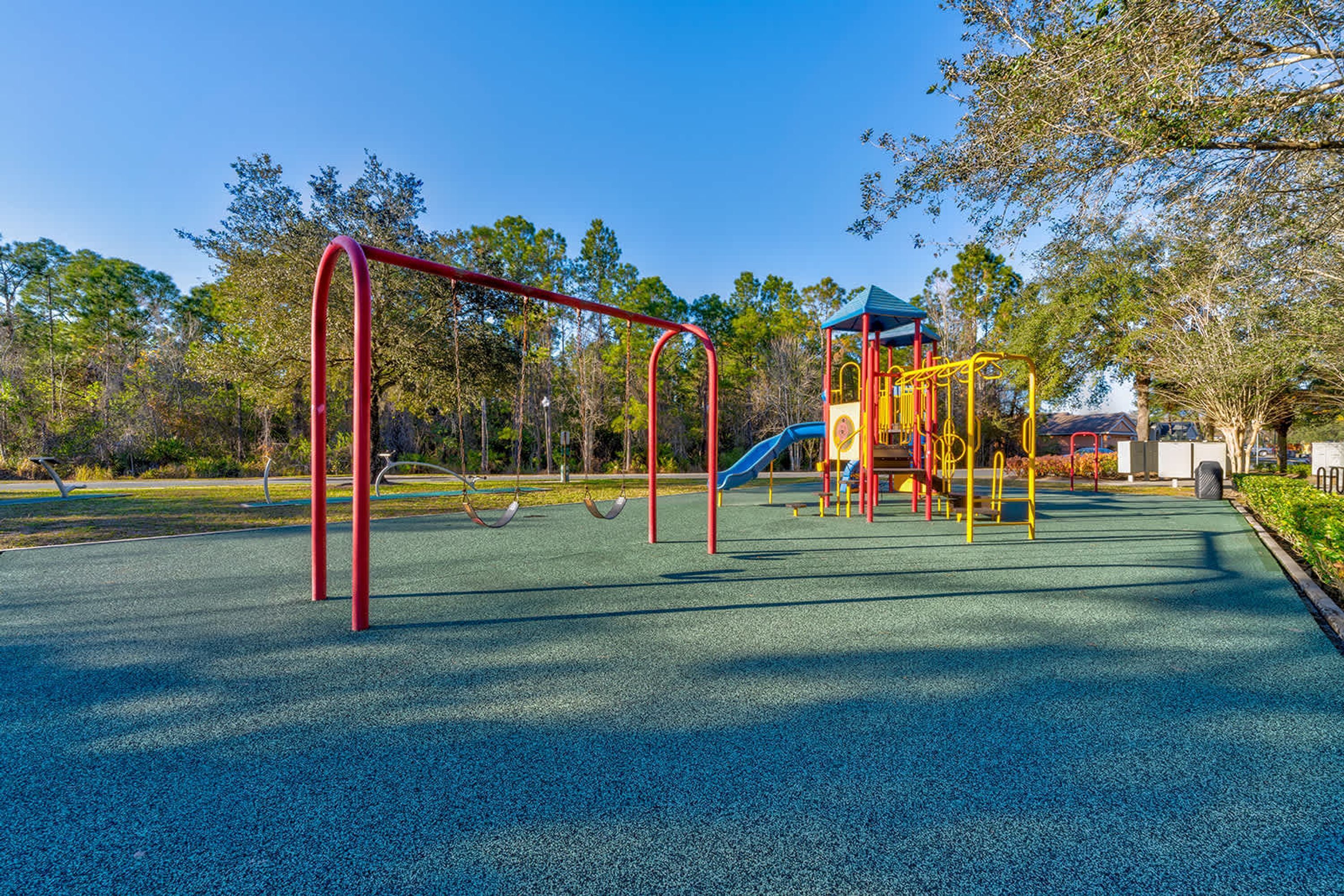 A playground with swings and a slide, surrounded by trees and a clear sky.