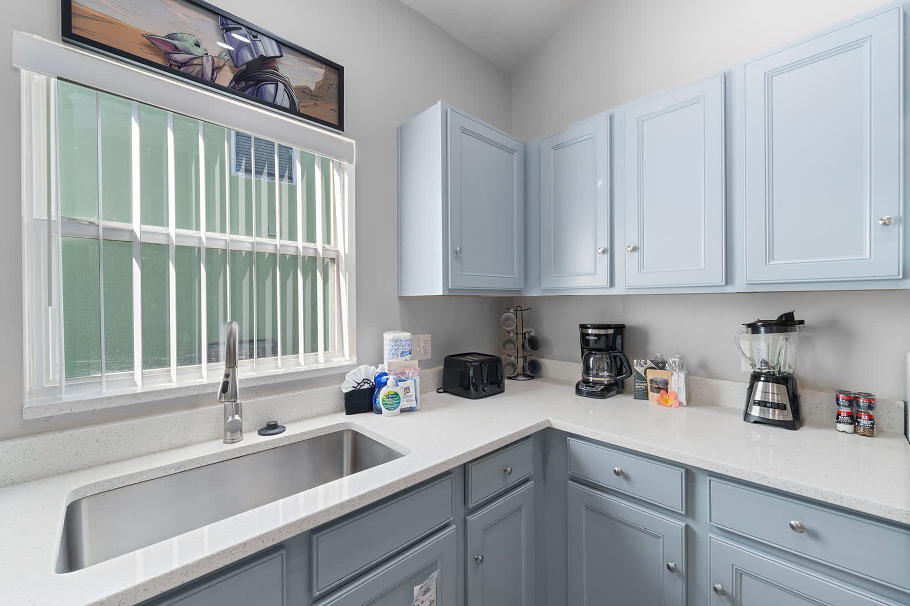 A kitchen with a sink, cabinets, a window, and various appliances.