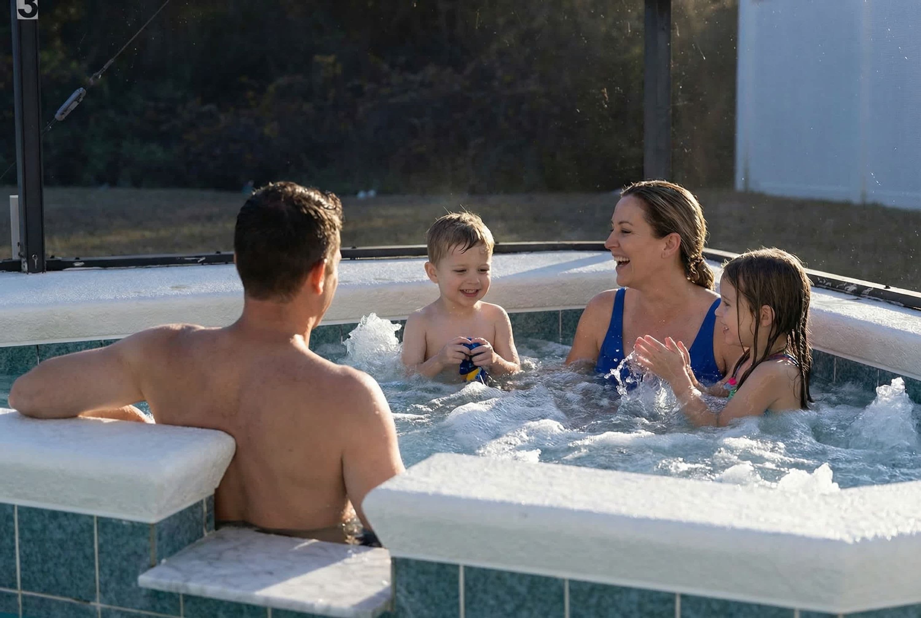 A family of four in a hot tub with a tiled exterior.
