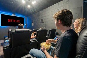 A movie theater with black leather seats, a large screen displaying 'NETFLIX', and a person holding a bowl of popcorn. - 12 min to Disney Movie Theater Pool In-ground spa (Davenport)