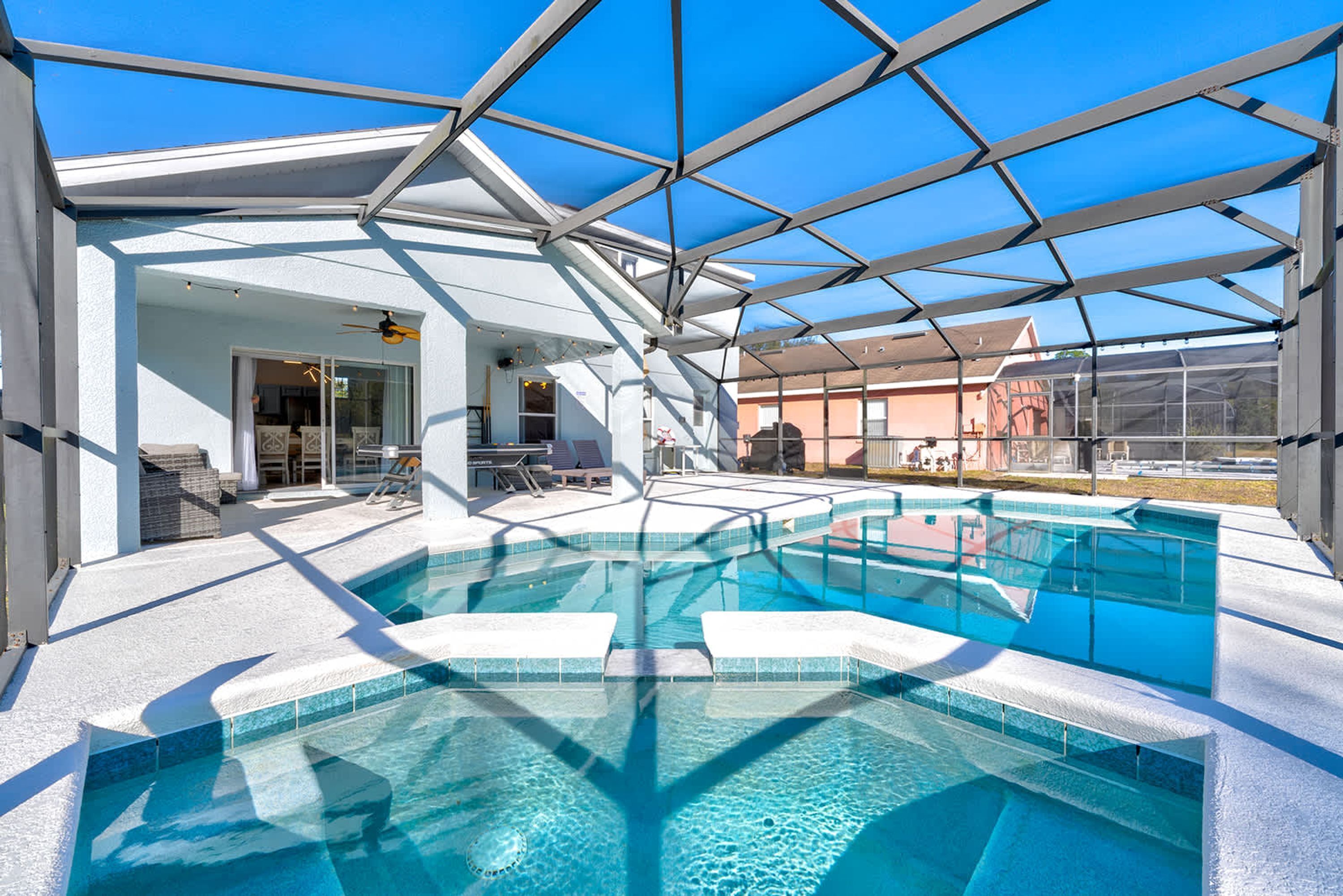 A covered outdoor swimming pool with a glass ceiling, surrounded by a white building with a patio area.